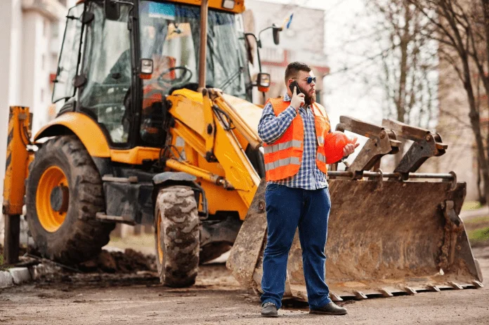 a person in a construction vest talking on a cell phone next to a bulldozer